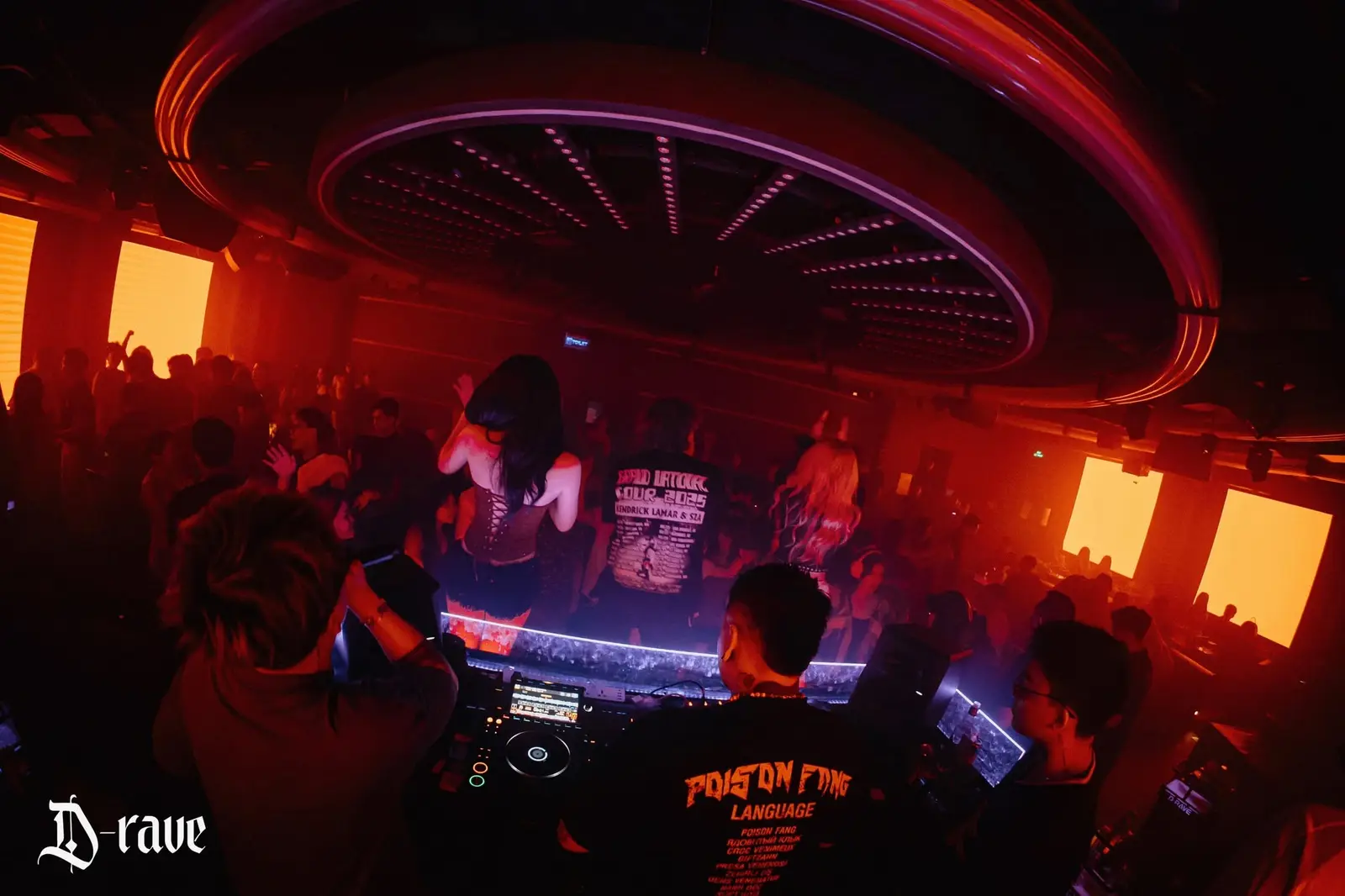 Bốt DJ viền đèn tím giữa phòng, các tấm LED cam sáng trên tường Drave Club