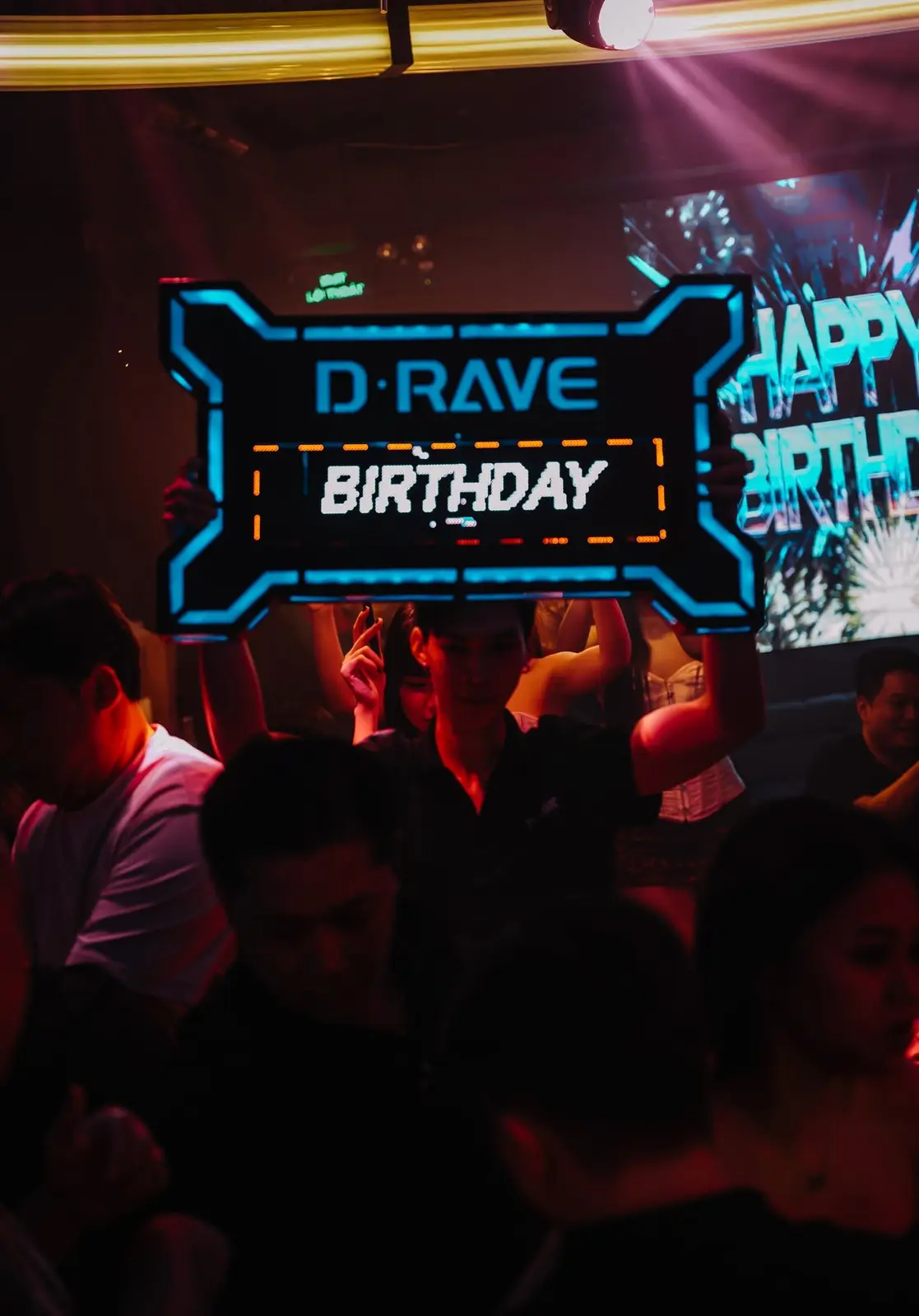Bảng đèn D·RAVE Birthday được giơ cao giữa đám đông, màn hình Happy Birthday phía sau